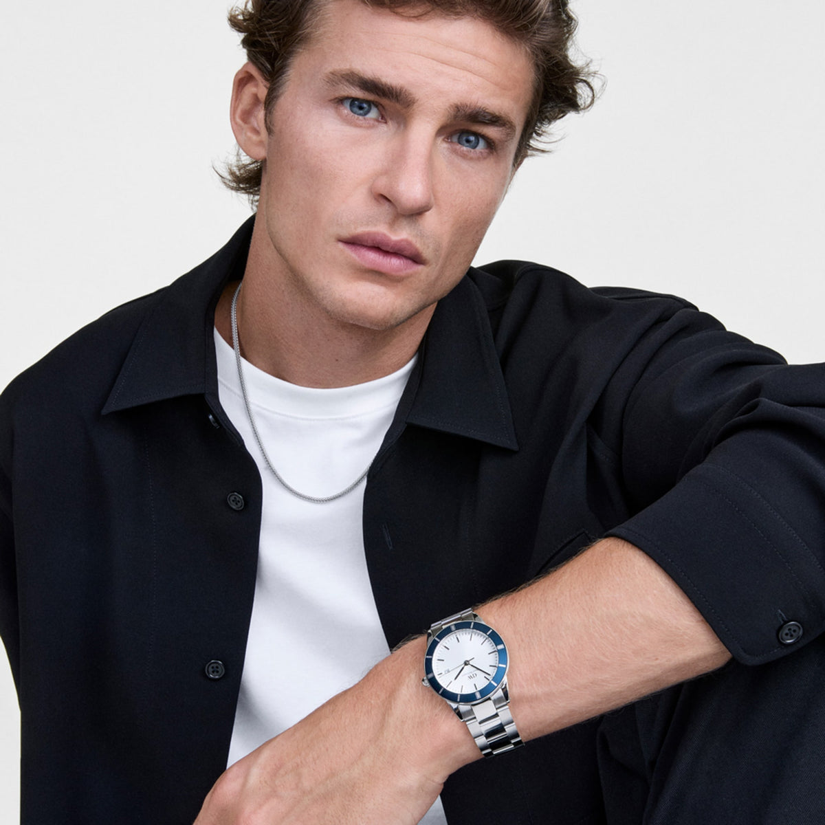 ダークネイビーのシャツと白Tシャツを合わせた男性が、Iconic Paradigma Link Blue Bezel Silverを着用しています。ブルーのベゼルとシルバーブレスレットが手元に爽やかなアクセントを加え、カジュアルなスタイリングに自然になじむデザインです。