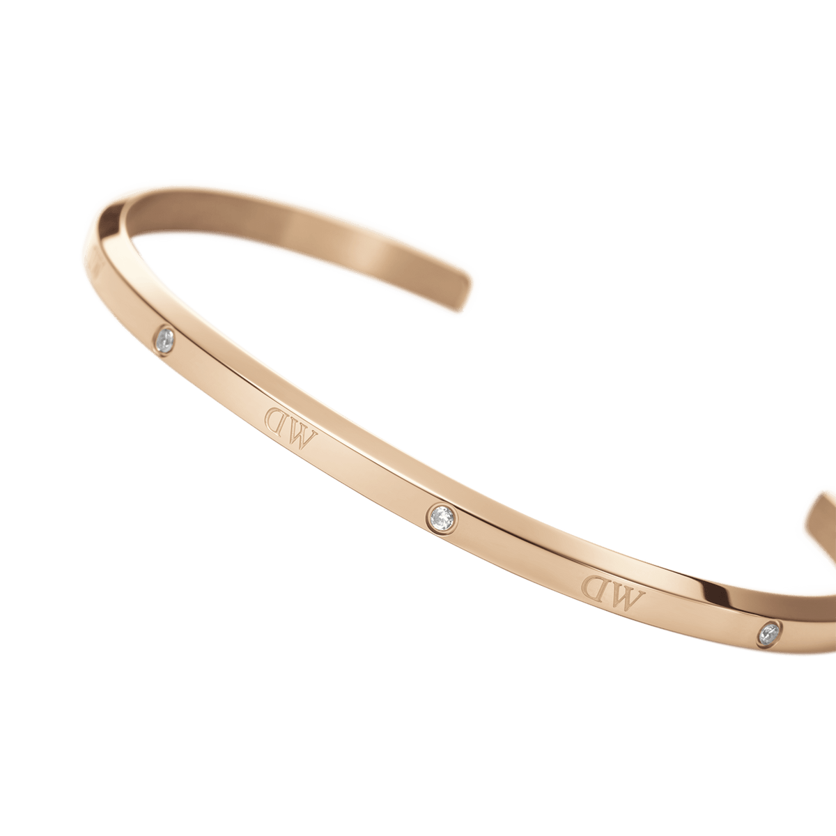 ローズゴールドのClassic Lumine Braceletをクローズアップで捉えた写真です。ポリッシュ仕上げの細身のカフには、Daniel Wellingtonのロゴとクリスタルが交互に配置され、光を受けて繊細な輝きを放っています。