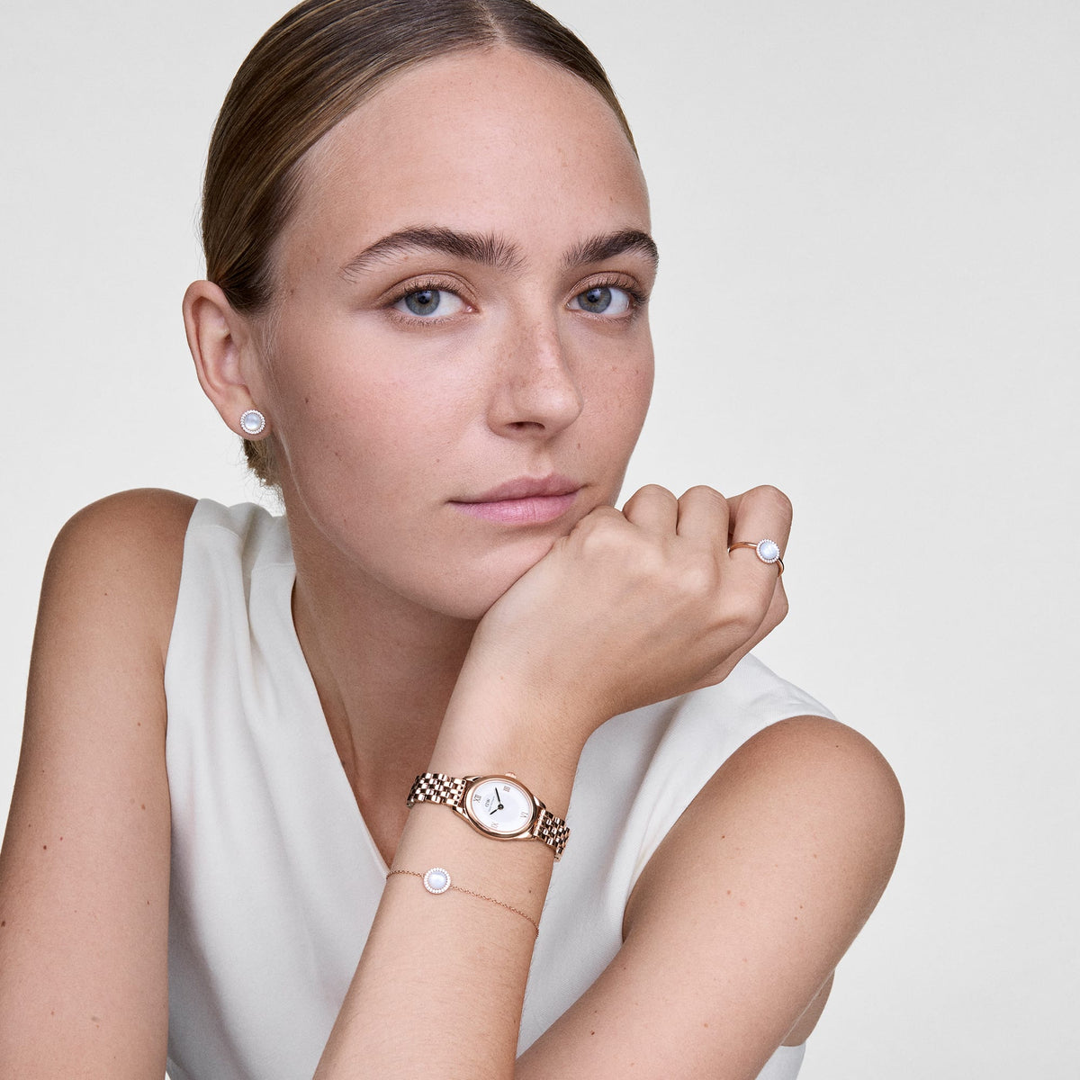 Audrey Ring Mother of Pearl Rose Goldを着用したスタイリングイメージです。同コレクションのイヤリングやブレスレット、ローズゴールドの腕時計と合わせ、マザーオブパールのトーンで統一したコーディネートをご紹介しています。