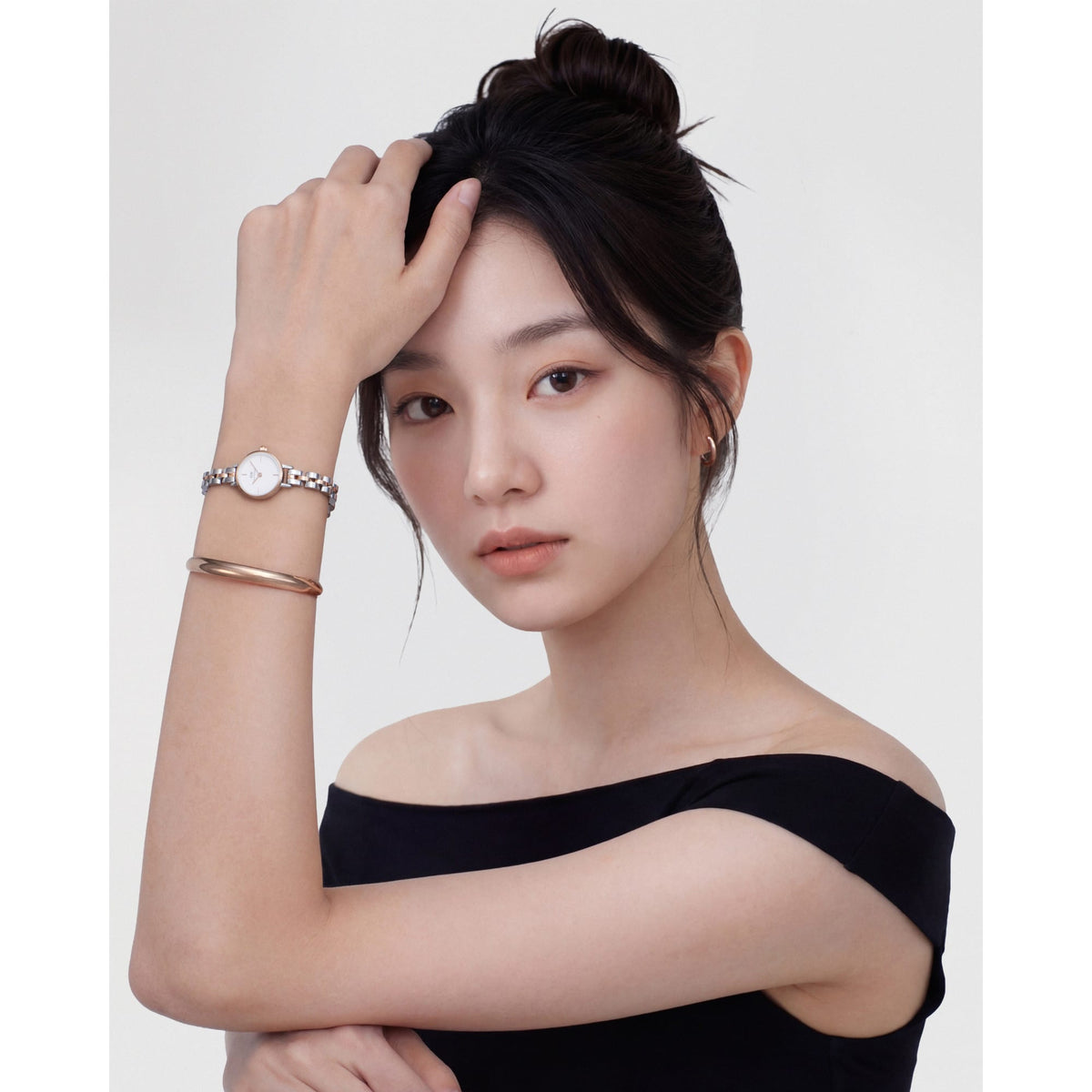 ブラックのオフショルダートップスを着た女性が、Arch Earrings Rose Gold 12mmを耳元に、Daniel Wellingtonの腕時計とローズゴールドのバングルを手首に重ね付けしたスタイリングです。