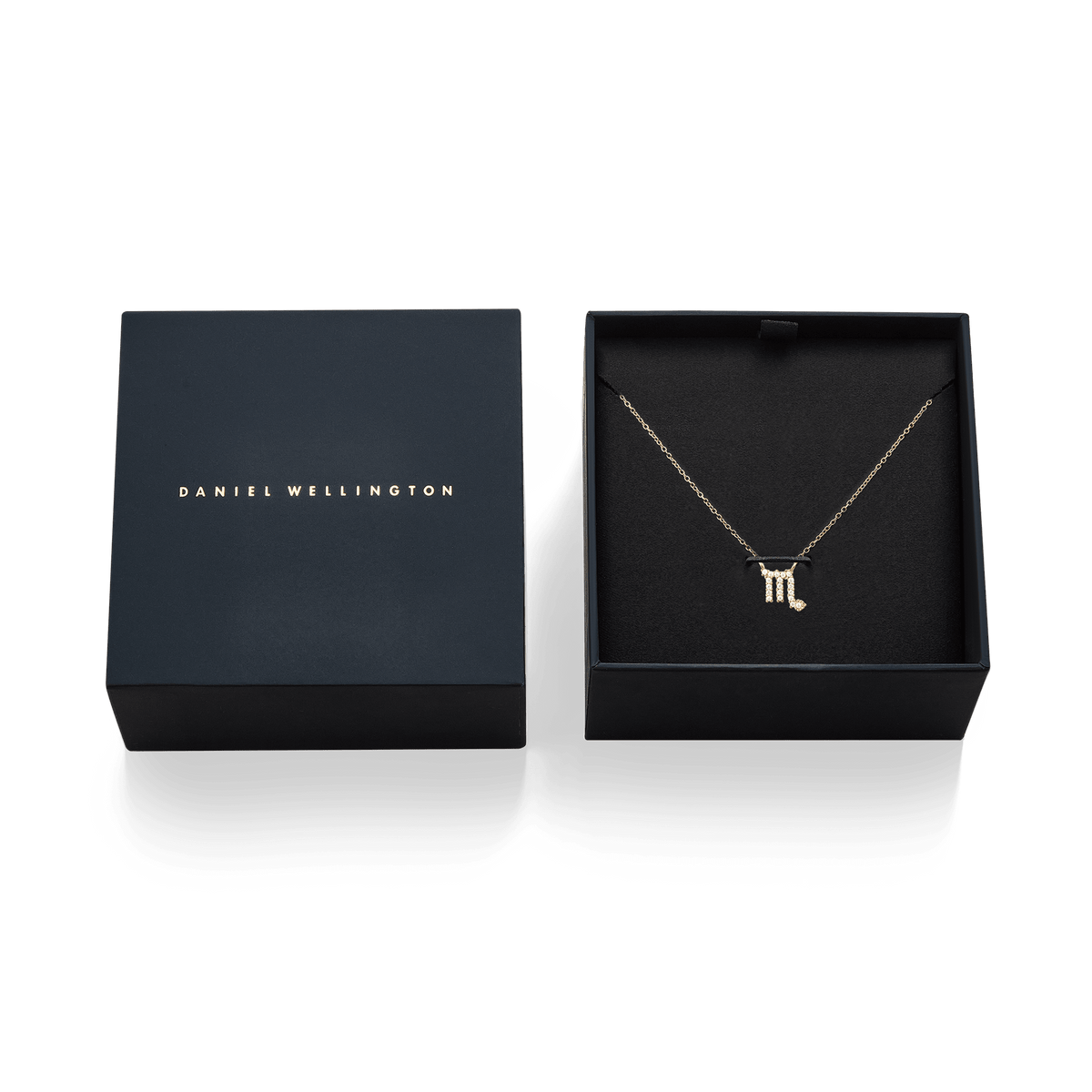 Daniel Wellingtonのネイビーギフトボックスに収められた、蠍座モチーフのCrystal Zodiac Chain Necklace Goldの俯瞰写真です。ブラックのクッション中央には、クリスタルで描かれた蠍座のシンボルをあしらったゴールドペンダントが丁寧に配置され、左側にはブランドロゴ入りの蓋が添えられています。