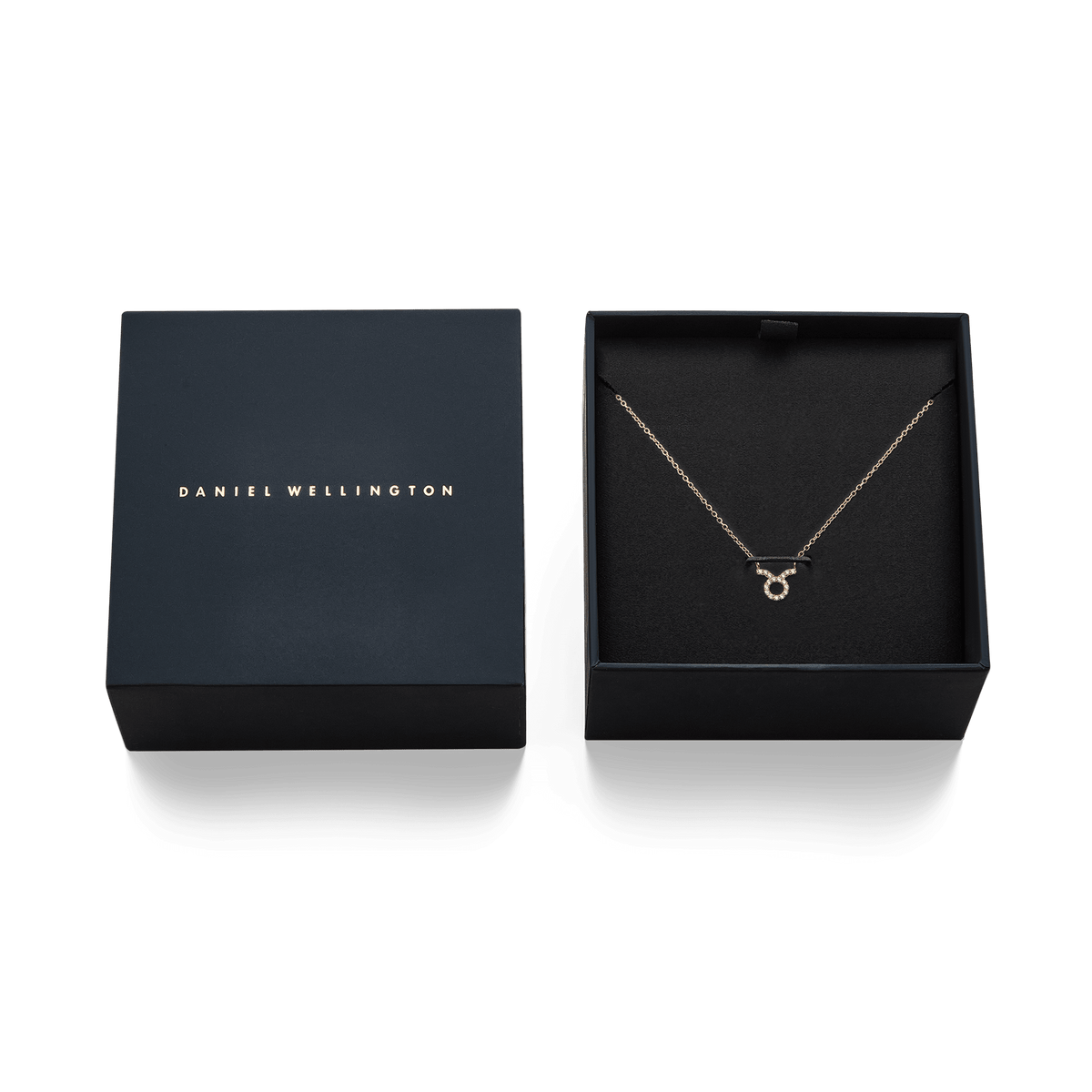 ダニエルウェリントンのネイビーギフトボックスに収められた、牡牛座モチーフのCrystal Zodiac Chain Necklace Goldの写真です。ブラックの内装にゴールドチェーンが映え、クリスタルをあしらった牡牛座のペンダントが中央に配置されています。隣にはブランドロゴ入りの蓋が添えられ、ギフトにぴったりの上品な仕上がりです。