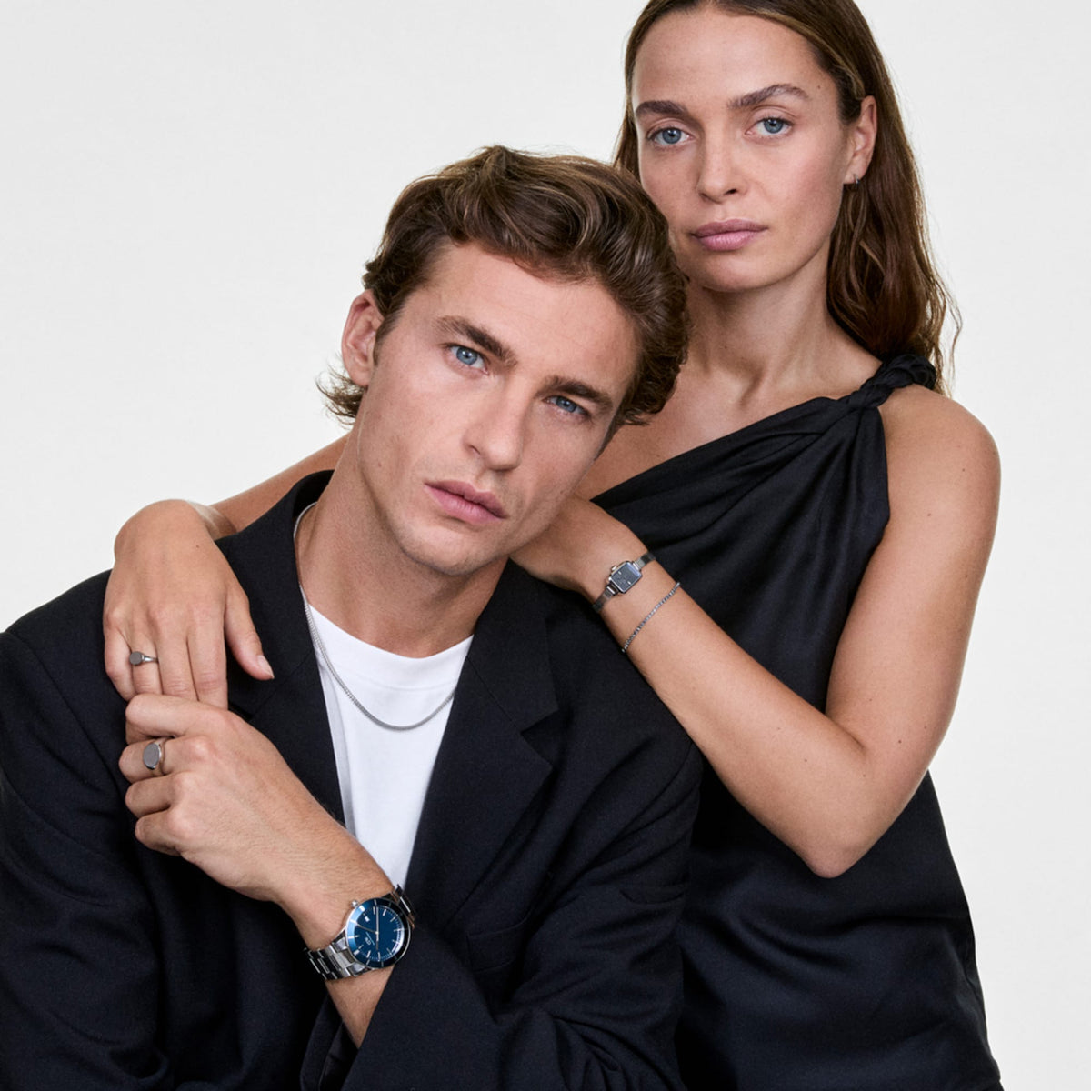 ダニエルウェリントンのTide Mesh Necklace Silverを男性が首元に着用し、シルバーリングや腕時計と合わせたスタイリング。女性はシルバーブレスレットとウォッチでペアルックを楽しんでいます。