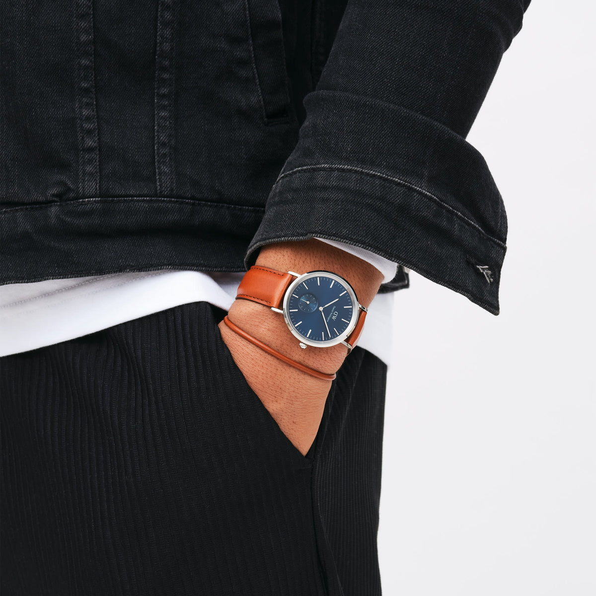 ブラウンレザーのSt Mawes Bracelet Silverを、同色のSt Mawesストラップを装着したシルバーケースの腕時計と重ね付けした着用例です。ブラックデニムジャケットとパンツのカジュアルなコーディネートに、ブラウンレザーの統一感が自然に映えます。