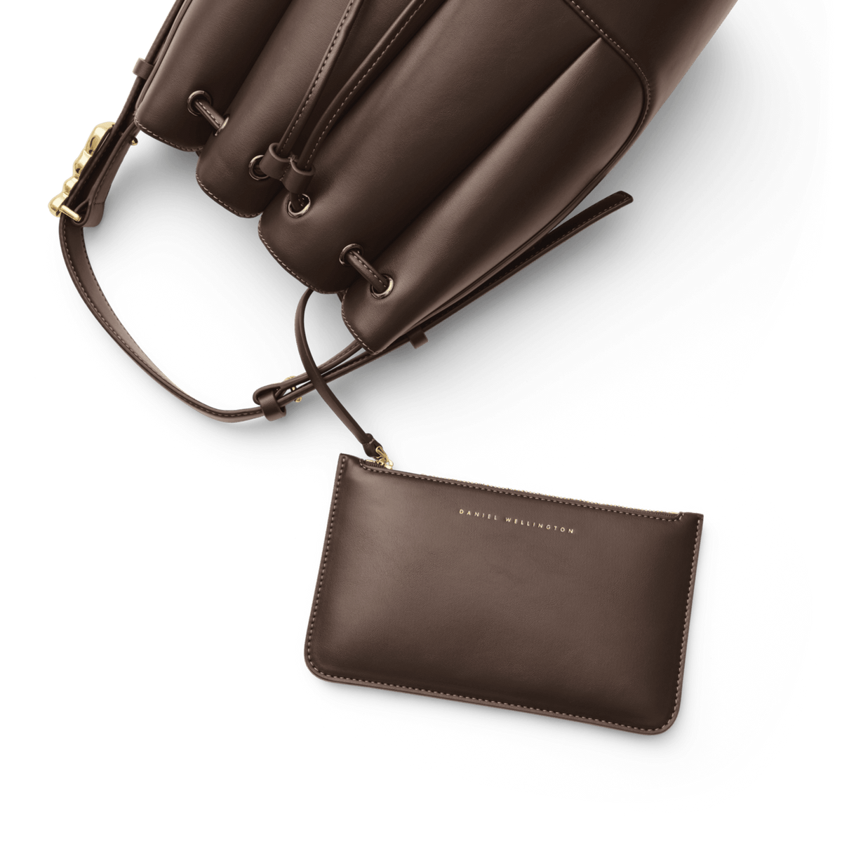 Lewis Bag Brownに付属するDaniel Wellingtonのロゴ入りポーチをクローズアップした画像です。バッグ本体のドローストリング部分にストラップで取り付けられたポーチが手前に広がり、同系色のブラウンエコレザーにはゴールドの箔押しロゴが上品にあしらわれています。