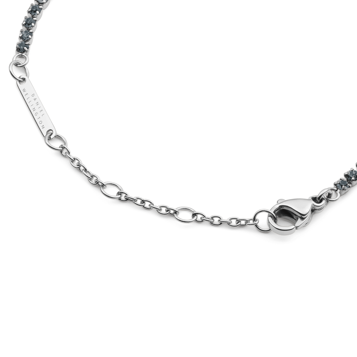 Classic Tennis Bracelet Nightfall Silverの留め具部分のディテール画像です。ロブスタークラスプとサイズ調節用のチェーン、Daniel Wellingtonの刻印が入ったブランドプレートが確認できます。また、両端にはダークトーンのクリスタルが連なっています。