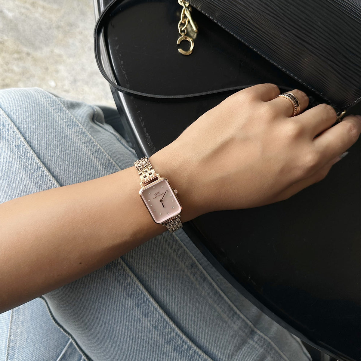 Quadro Lumine 5 Link Melrose Pink MoP Rose Goldを着用した手元のスタイリングです。ライトデニムとブラックレザーバッグに合わせ、ローズゴールドのリングと重ね付けすることで、カジュアルながら上品な印象に仕上げています。