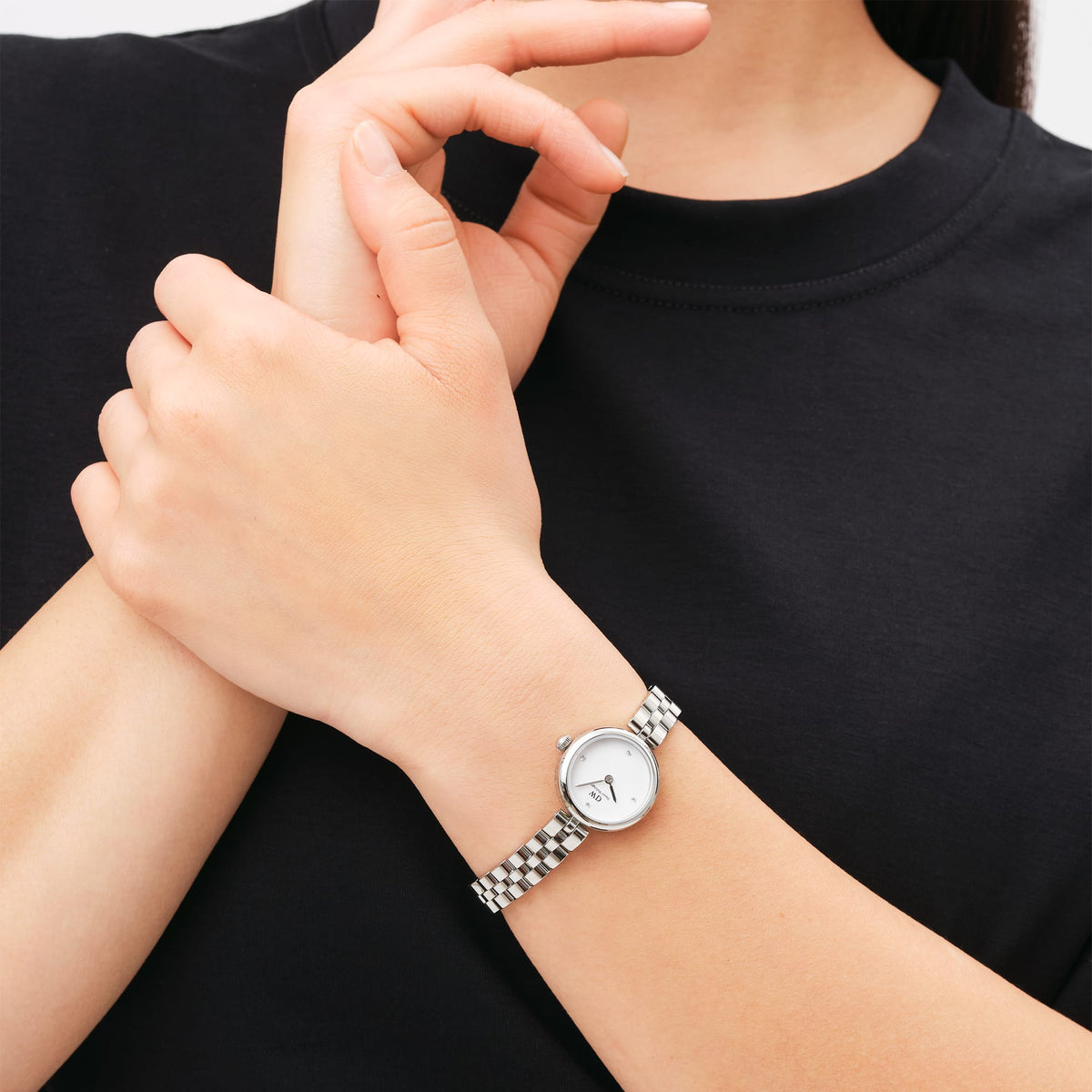 Elan Lumine Silverを手首に着けた女性のクローズアップです。ブラックのトップスに映えるシルバーの3連ブレスレットと、コンパクトなホワイトダイヤルが手元に上品な輝きを添え、ブレスレット感覚で身に着けられます。