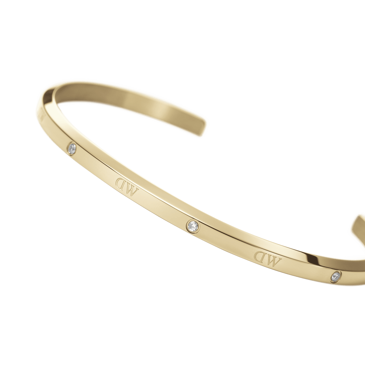 Daniel Wellington Classic Lumine Braceletのゴールドカフを近距離で撮影したクローズアップ画像です。滑らかなポリッシュ加工の表面に刻印されたロゴと、ベゼルセッティングで留められたクリスタルの細やかなディテールが際立ちます。