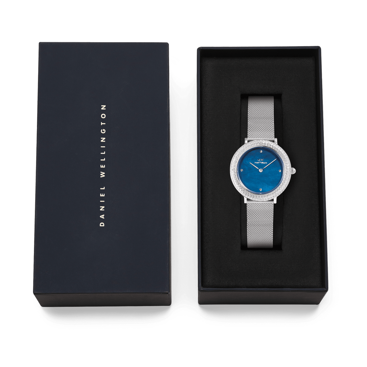 Daniel Wellingtonのネイビー色のブランドボックスに収められたCrystalline Bezel Sterling Blueのギフトセットです。ブラックのクッショニング上に、シルバーメッシュストラップとブルーマザーオブパールダイヤルの腕時計が丁寧にセットされており、贈り物にぴったりの上品な仕上がりとなっています。