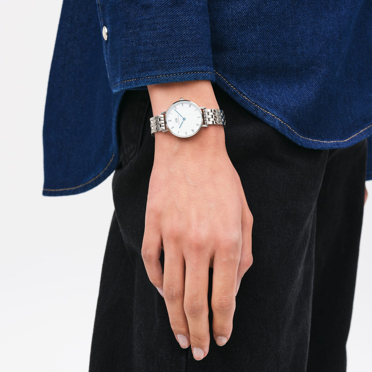 Petite Roman Numerals 5-Link Silverを手首に着用したスタイリング例です。デニムシャツとダークパンツのカジュアルなコーディネートに、シルバーの5リンクブレスレットとブルースチールの針が映える28mmのコンパクトサイズがよく合います。