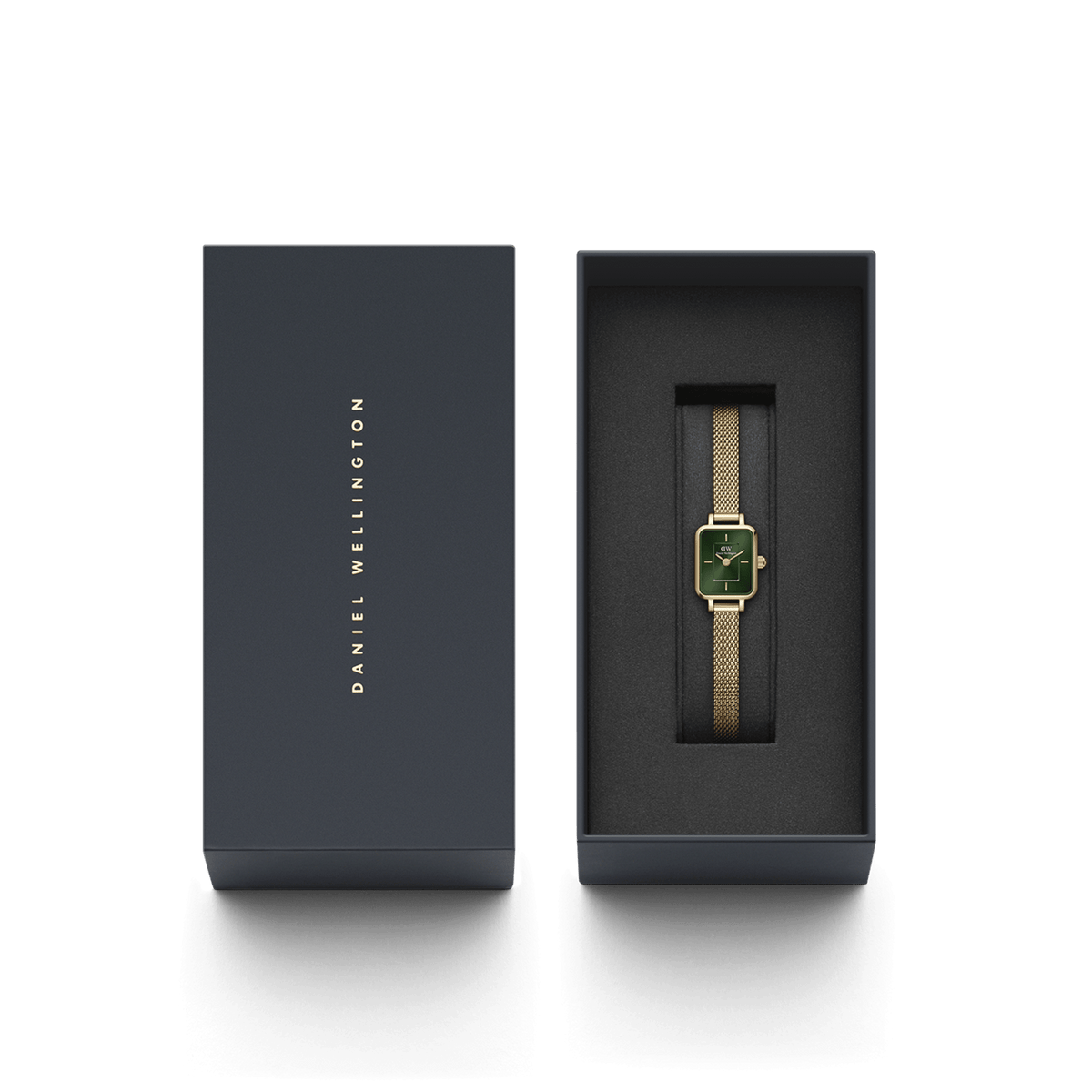Quadro Mini Evergold Emeraldがダークグレーの専用ギフトボックスに収められた様子です。蓋にはDaniel Wellingtonのロゴがゴールドで刻印され、ゴールドメッシュのストラップとエメラルドグリーンの文字盤が黒いクッションカバーの上で美しく映えています。