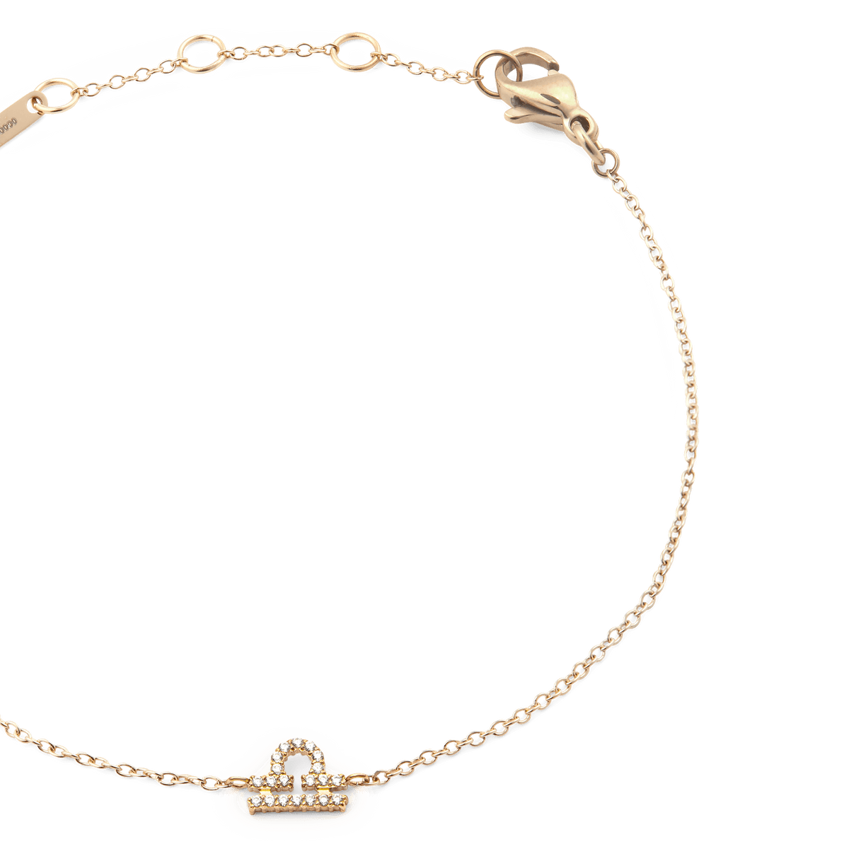 天秤座モデルのCrystal Zodiac Chain Bracelet Goldを斜め上から撮影したクローズアップ画像です。ゴールドの細いチェーンが優美なカーブを描き、中央にはクリスタルであしらわれた天秤座のモチーフが光を反射して繊細に輝いています。右上にはロブスタークラスプ、左上にはブランド刻印プレートとアジャスターリングが確認できます。