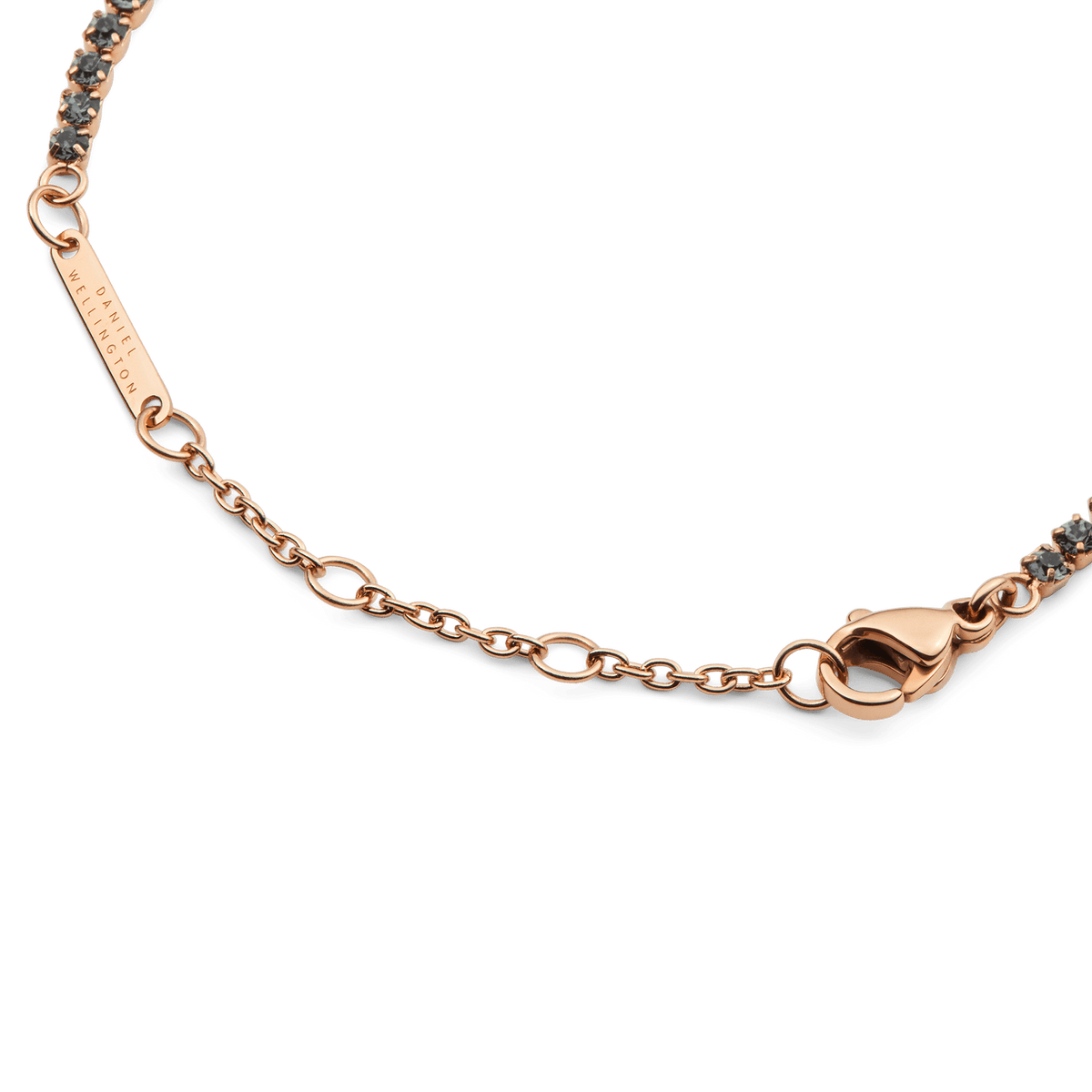 Classic Tennis Bracelet Nightfall Rose Goldのサイズ調整用チェーン部分を拡大した画像です。Daniel Wellingtonの刻印が施されたローズゴールドのプレート、小判チェーン、ロブスタークラスプの細部まで確認できます。また、両端に続くダークトーンのクリスタルもご覧いただけます。