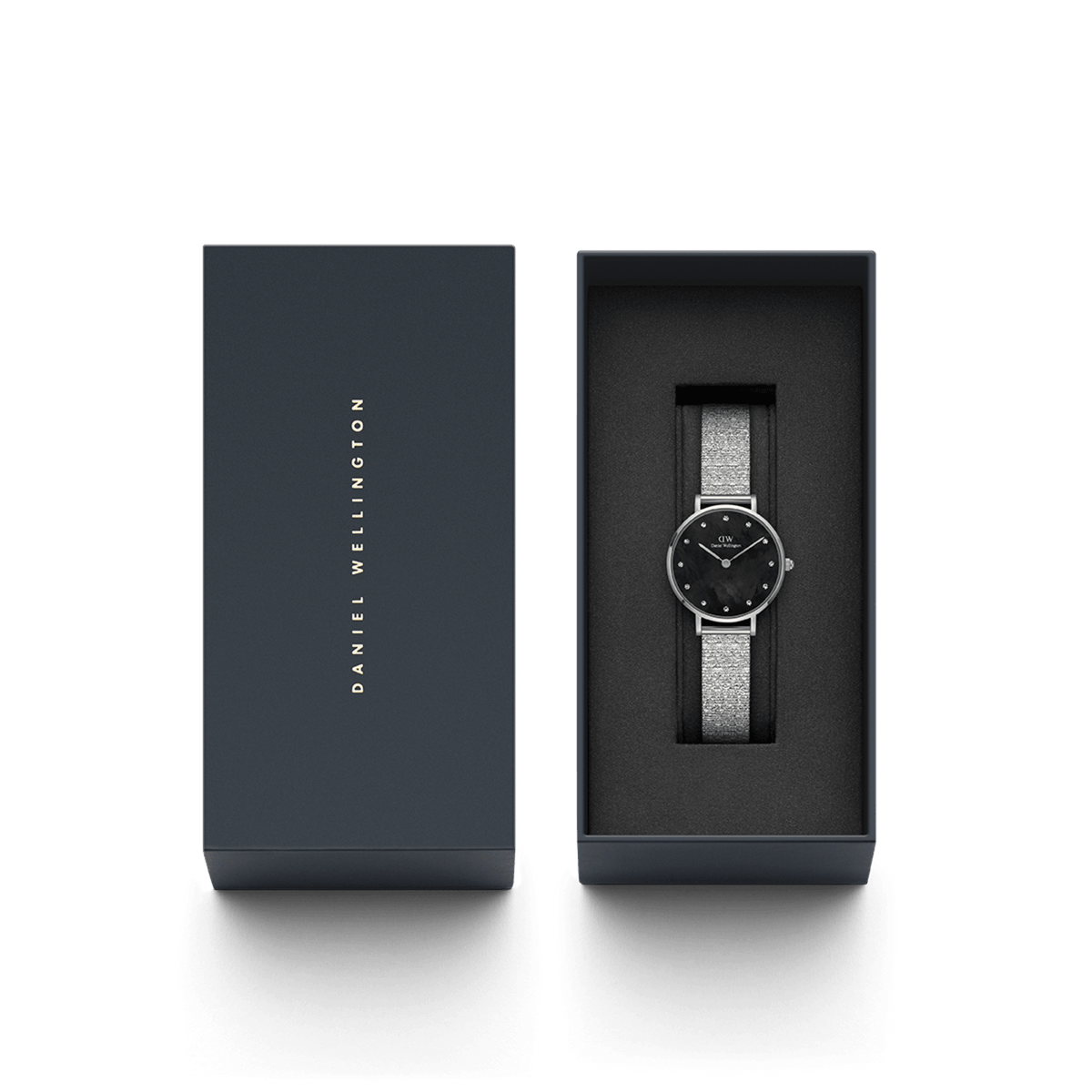 Petite Lumine Pressed Piano Black MoP Silverが、ダークネイビーのブランドギフトボックスに収められています。箱の蓋にはDaniel Wellingtonのロゴがゴールドで刻印され、ブラックマザーオブパールの文字盤とシルバーのPressed Pianoストラップが黒いクッションの上で美しく輝いています。