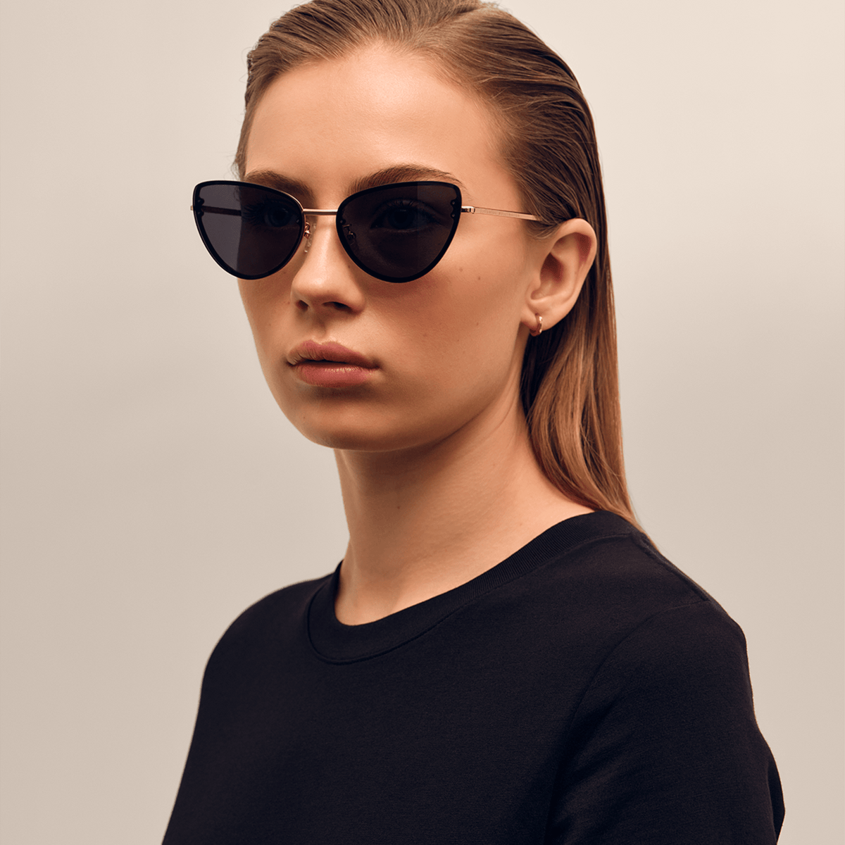 Daniel Wellington Lynx Steel Blackを着用した女性モデルの斜めアングル写真です。ブラックのクルーネックトップスにキャットアイシルエットのサングラスを合わせ、ローズゴールドの細身テンプルが横顔に沿うスタイリングが特徴です。