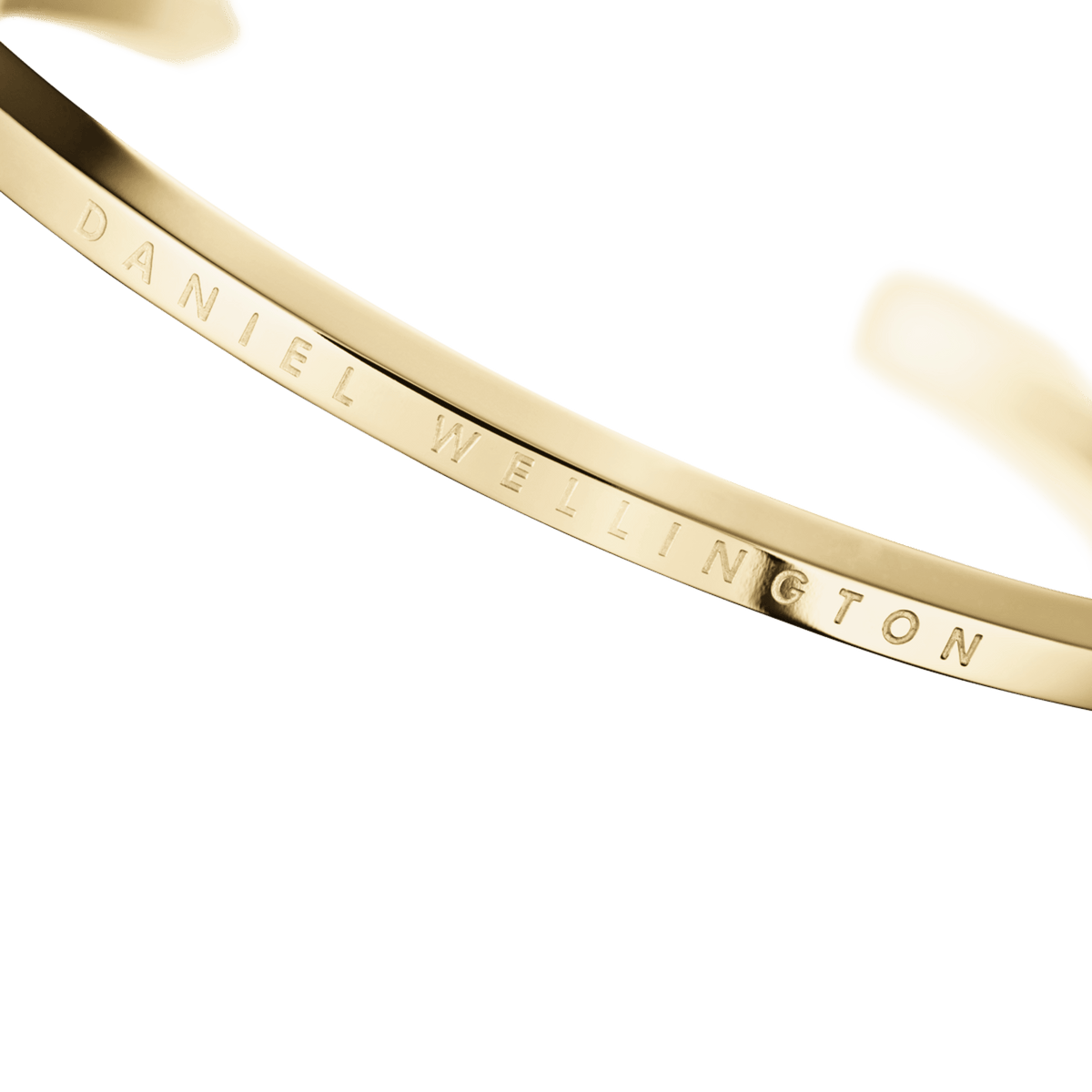 Classic Bracelet Goldのロゴ刻印部分をクローズアップした画像です。ポリッシュ仕上げのゴールドカフ表面に、Daniel Wellingtonの文字が繊細に刻印されているディテールがご覧いただけます。