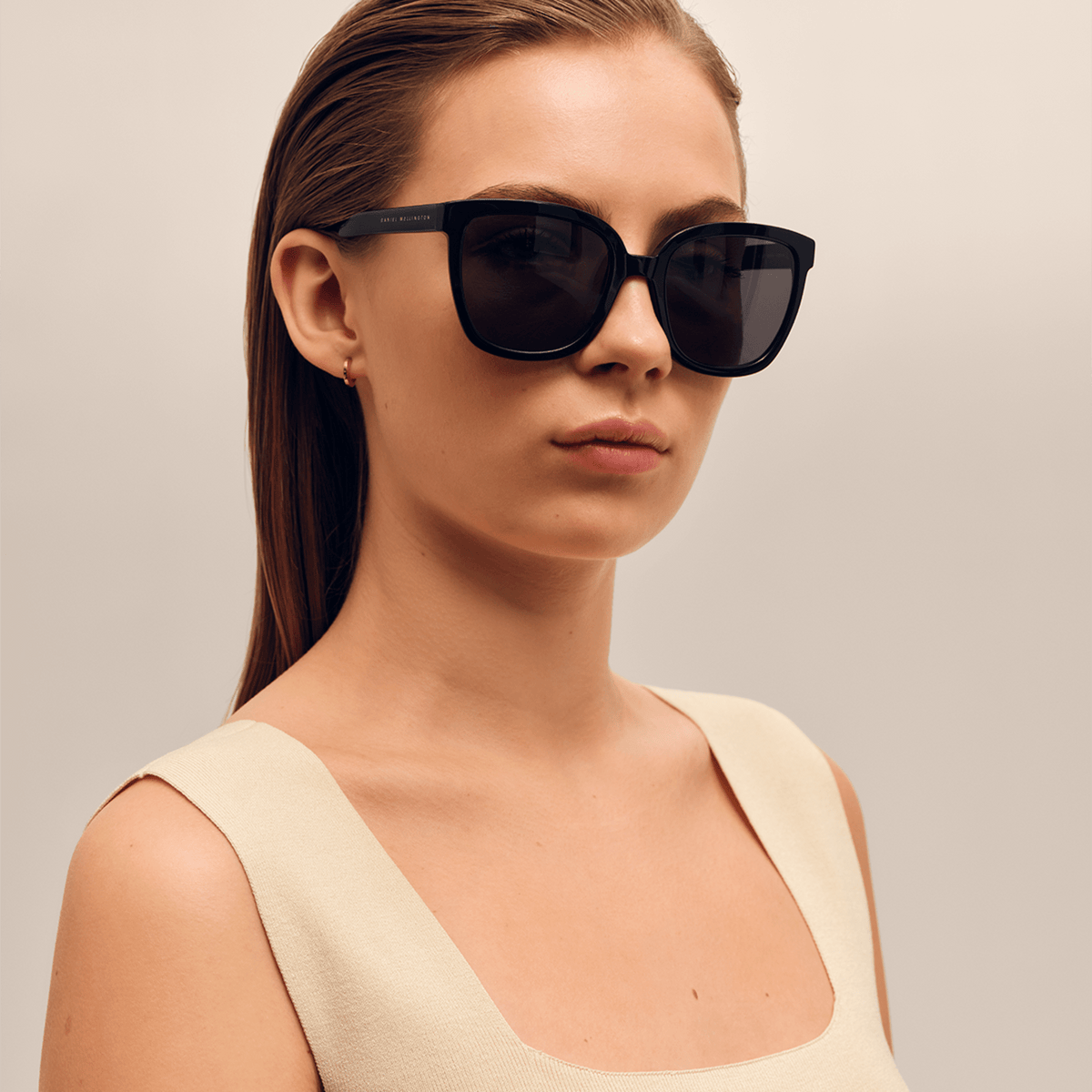ダニエルウェリントンのGrande Bio-Acetate Blackを着用した女性モデル。ブラックのオーバーサイズフレームが顔周りにゆったりとしたシルエットを描き、ベージュのトップスと合わせることで洗練された印象を演出しています。