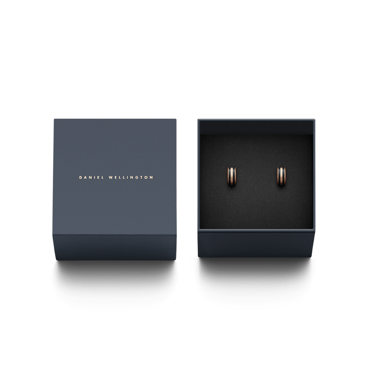 Daniel Wellingtonのロゴが箔押しされたネイビーの専用ギフトボックスに収められたEmalie Earrings Rose Gold Black。ブラックエナメルとローズゴールドのコントラストが美しい小ぶりなフープピアスが、ブラックのクッション上に丁寧にセットされています。