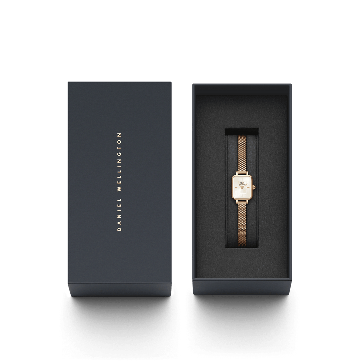 Daniel Wellingtonのギフトボックス入りQuadro Mini Melrose。ネイビーカラーのボックスにゴールドのブランドロゴが箔押しされ、黒いクッショニングの上にローズゴールドのメッシュストラップとスクエアケースが美しく収められています。贈り物にぴったりの上品なパッケージです。