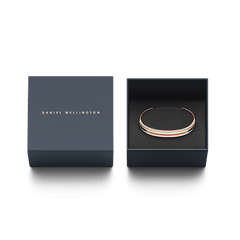 Daniel WellingtonのEmalie Slim Bracelet ローズゴールドが、ネイビーのギフトボックスに収められています。箔押しされたブランドロゴの蓋と、黒いクッションケースに丁寧にセットされたブレスレットは、贈り物にぴったりの上品な仕上がりです。