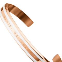 Emalie Slim Braceletを斜めから捉えたアングルの画像です。ローズゴールドの輝きとサテンホワイトのエナメルラインのコントラスト、そしてDaniel Wellingtonのロゴ刻印が美しく映えるカフブレスレットのディテールをご覧いただけます。