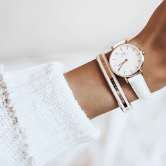 白いニットの袖口からのぞく手首に、ホワイトレザーストラップのローズゴールド腕時計とEmalie Bracelet Satin White Rose Goldを重ね付けしたコーディネート。ホワイトとローズゴールドの組み合わせが、柔らかな雰囲気の装いに上品な輝きを添えています。