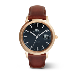 Daniel WellingtonのIconic St Mawes Automatic Rose Goldです。ローズゴールドのケースにブラック文字盤を採用し、3時位置には日付表示窓を配しています。夜光インデックスと針で暗所でも時刻が確認でき、ブラウンのレザーストラップが上品な印象を演出します。自動巻き機能を搭載した腕時計です。