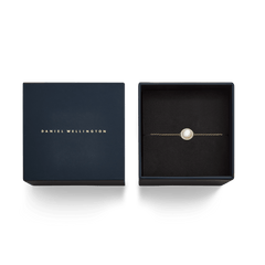 ダニエルウェリントンのAudrey Bracelet Mother of Pearl Goldは、ネイビーカラーのギフトボックスに収められています。箔押しされたブランドロゴの蓋と、黒いクッションケースに丁寧にセットされたマザーオブパールのチャーム付きゴールドチェーンブレスレットが、特別な贈り物にぴったりの上品なパッケージです。