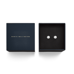 ダニエルウェリントンのネイビーカラーのギフトボックスに収められたAudrey Earrings Mother of Pearl Silverのパッケージ画像です。ゴールドのブランドロゴがあしらわれた蓋と、黒いクッションの上に並ぶマザーオブパールのスタッドピアスが、贈り物にぴったりの上品な佇まいを演出しています。