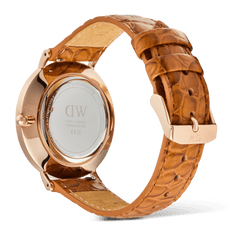Daniel Wellington Classic Roman Numerals Dateの裏面を捉えたアングルです。ローズゴールドケースの裏蓋にはブランドロゴやシリアルナンバーが刻印されており、ライトブラウンのクロコダイル調レザーストラップのローズゴールドピンバックルにはDWの刻印が施されています。