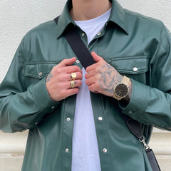 グリーンのレザージャケットにゴールドのリングを合わせたストリートスタイルに、Daniel Wellington Classic Mesh Onyx Goldを着用した男性のコーディネート例です。ブラックダイヤルとゴールドメッシュベルトが、手元に控えめながらも存在感を演出します。