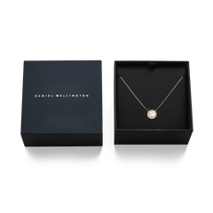 Audrey Necklace Mother of Pearl Rose Goldが、Daniel Wellingtonのネイビーブランドギフトボックスに収められています。黒いクッションの上にローズゴールドチェーンとマザーオブパールのペンダントが美しく配置され、贈り物にぴったりの上品なパッケージです。