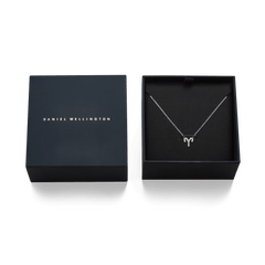 おひつじ座をモチーフにしたCrystal Zodiac Chain Necklace Silverが、Daniel Wellingtonのネイビーカラーギフトボックスに収められた様子です。ボックスの蓋にはブランドロゴがゴールドで刻印され、ブラックの内装にクリスタルの輝きを放つペンダントが映えるギフト仕様となっています。