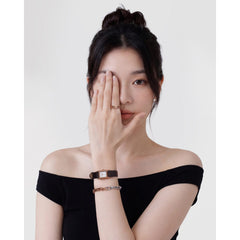 Contrast Link Bracelet Two Tone Rose Goldを腕時計やリングと重ねづけした女性のスタイリングです。ブラックのオフショルダー・トップスに、ローズゴールドとシルバーのツートーンブレスレットが映え、洗練された印象を演出しています。