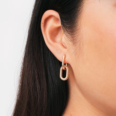 Daniel WellingtonのCrystal Link Earrings Rose Goldを着用したクローズアップ画像です。ローズゴールドのフープから繋がるオーバルリンクにあしらわれたクリスタルが、耳元で煌めきながら揺れます。肌になじむ温かみのある色合いが上品な印象を与えます。