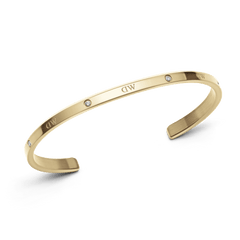 クラシックなLumine Braceletゴールドを斜めから撮影した製品写真です。ベゼルセッティングのクリスタルとブランドロゴが交互に並ぶポリッシュ仕上げの表面と、サテン仕上げの内側の質感の違いがわかるオープンカフデザインとなっています。