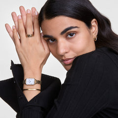Daniel Wellington Classic Bracelet Goldをゴールドの腕時計やリングと重ね付けしたスタイリング例です。黒のニットに映えるゴールドジュエリーの組み合わせで、手元に統一感のある上品な印象を演出します。