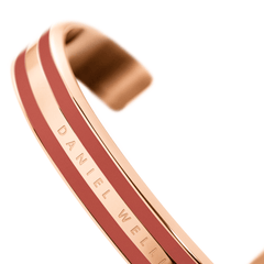Emalie Bracelet Cherry Blush Rose Goldを手前にピントを合わせ、背景をぼかしたアングルで撮影した画像です。二本のチェリーブラッシュエナメルラインの間に刻印されたDaniel Wellingtonのロゴと、ローズゴールドのダブルレイヤーカフの立体感が際立ちます。