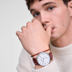 クラシックなマルチアイデザインのSt Mawes Off-white Sunray Silverを着用した男性モデル。ブラウンのレザーストラップとレザーブレスレットを重ね付けし、白いニットに合わせたカジュアルスタイルです。