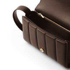 Daniel WellingtonのSadie Bag Brownのフラップを開いた内部をクローズアップした画像です。ゴールドファスナー付きの内ポケットやマグネット式のフラップ留め具、そして立体感のある縦パフキルティングのディテールが確認できます。