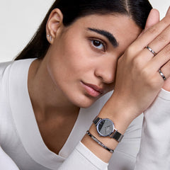 シルバーメッシュストラップのPetite ReflectionとClassic Lumine Braceletを重ね付けした女性の着用イメージです。白いVネックトップスに合わせ、手元をシルバートーンで統一したスタイリングをお楽しみいただけます。
