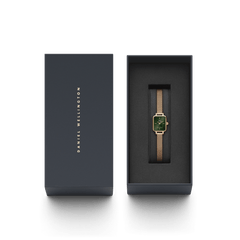 Quadro Mini Melrose Emeraldがダークグレーの専用ギフトボックスに収められています。箱の蓋にはDaniel Wellingtonのロゴが箔押しされ、内側のクッションにはエメラルドグリーンの文字盤を持つローズゴールドの腕時計が丁寧にセットされており、贈り物にぴったりの上品なパッケージです。