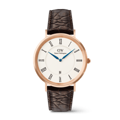Daniel Wellington Classic Roman Numerals Dateの正面画像。ローズゴールドのケースにホワイト文字盤、ローマ数字のインデックス、ブルーの時分針、6時位置の日付表示窓を備え、ダークブラウンのクロコダイル風レザーストラップを合わせたデザインです。