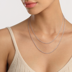 Daniel WellingtonのTwisted Chain Necklace Sを2本重ねて着用したスタイリング例です。異なる長さのシルバートーンチェーンが鎖骨から胸元にかけて美しいレイヤード効果を演出し、ベージュのニットトップスとも自然に調和します。