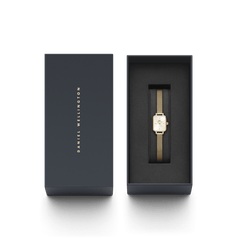 Quadro Mini Evergold Champagneがダークネイビーの専用ギフトボックスに収められた様子です。ボックスの蓋にはDaniel Wellingtonのロゴがゴールドで刻印され、ゴールドメッシュストラップのミニスクエアウォッチが黒いクッションの上にセットされています。