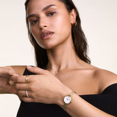 女性がDaniel WellingtonのPetite Miniゴールドメッシュ腕時計を左手首に、Pave Crystal Ringを右手の薬指に着用したスタイリングイメージです。ブラックのオフショルダートップに合わせ、ゴールドトーンのアクセサリーが手元に統一感を演出しています。