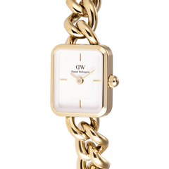 Jolie Chain Goldのダイヤル部分を斜めから捉えたクローズアップ画像です。ゴールドのスクエアケースに収まるホワイトエンボスダイヤルには、バーインデックスと針の繊細なディテールが際立ち、右側のリューズやケースから続くカーブチェーンリンクの美しい光沢もご覧いただけます。