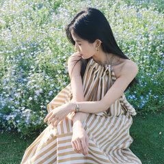 ネモフィラの花畑で、ストライプのワンピースを着た女性がQuadro Mini Evergold Emeraldを手首に着用したスタイリングイメージです。小ぶりなゴールドケースとエメラルドグリーンの文字盤が、自然光の下できらめきます。