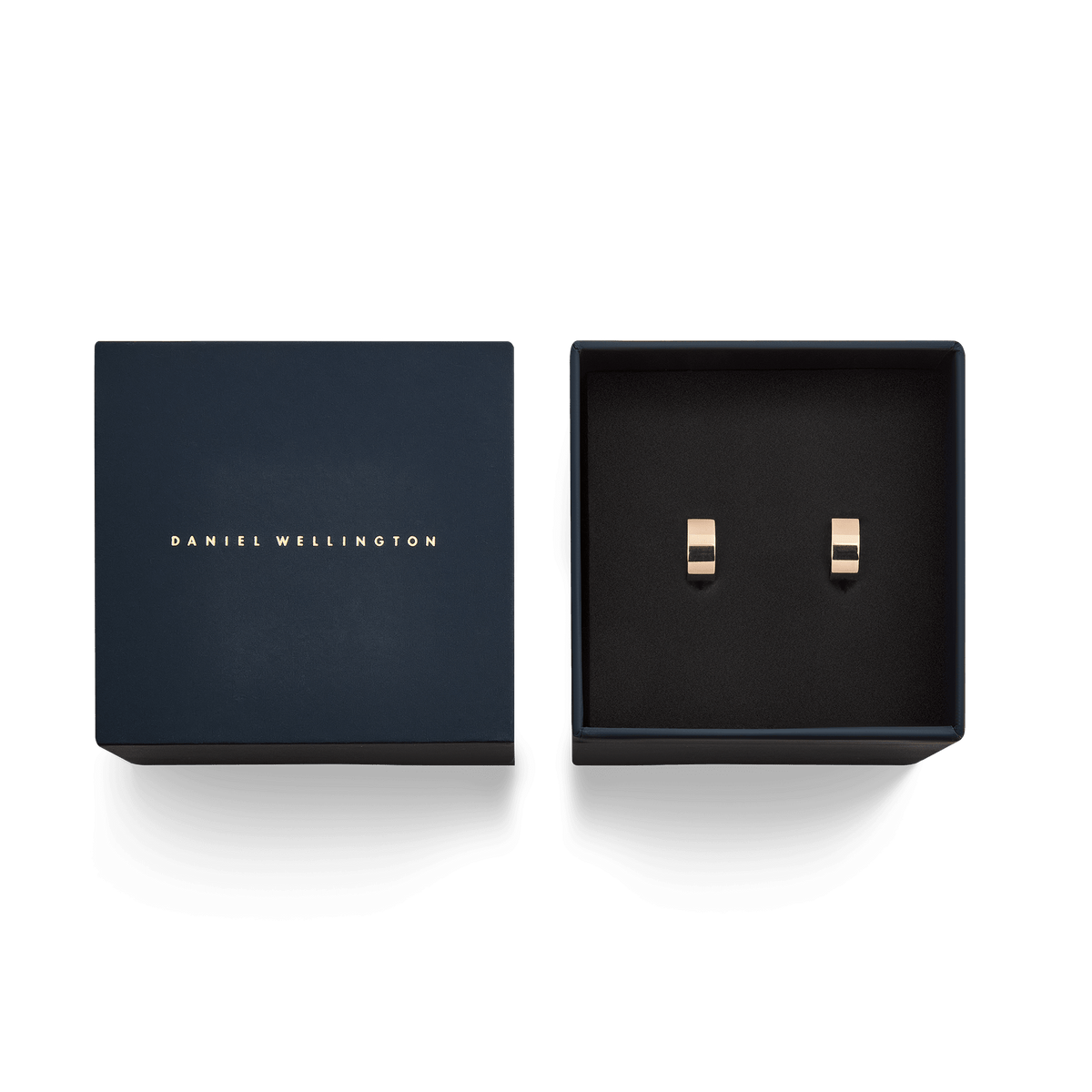 Daniel Wellingtonのネイビーブルーのギフトボックスに収められたLine Earrings ローズゴールド。箔押しのブランドロゴが施された蓋と、黒いクッションの上に並ぶ小ぶりなフープピアスは、贈り物にぴったりの上品な佇まいです。